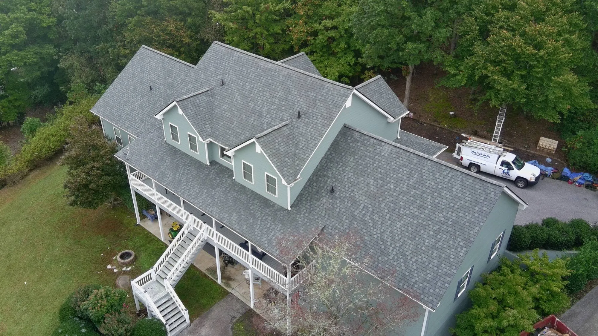 Drone view of the same home after Iron Ridge installed a new gray shingle roof, with the Iron Ridge Roofing truck in the driveway