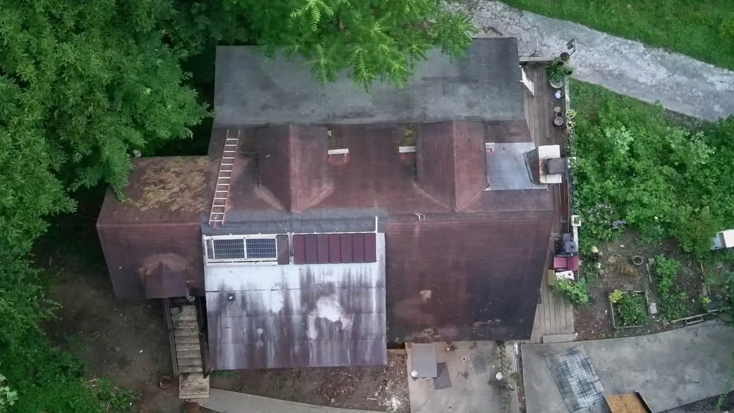 Top-down drone view of a home before replacement: an old roof with moss, rust stains, and patched sections