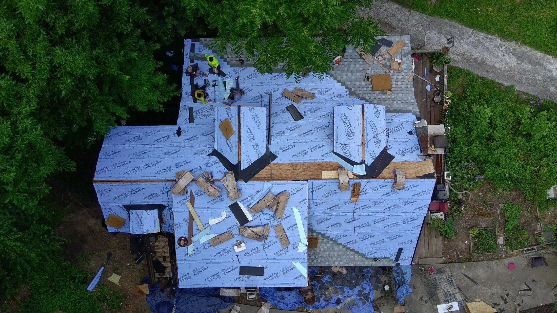 Iron Ridge crew installing new underlayment on a roof, with tarps protecting the yard below