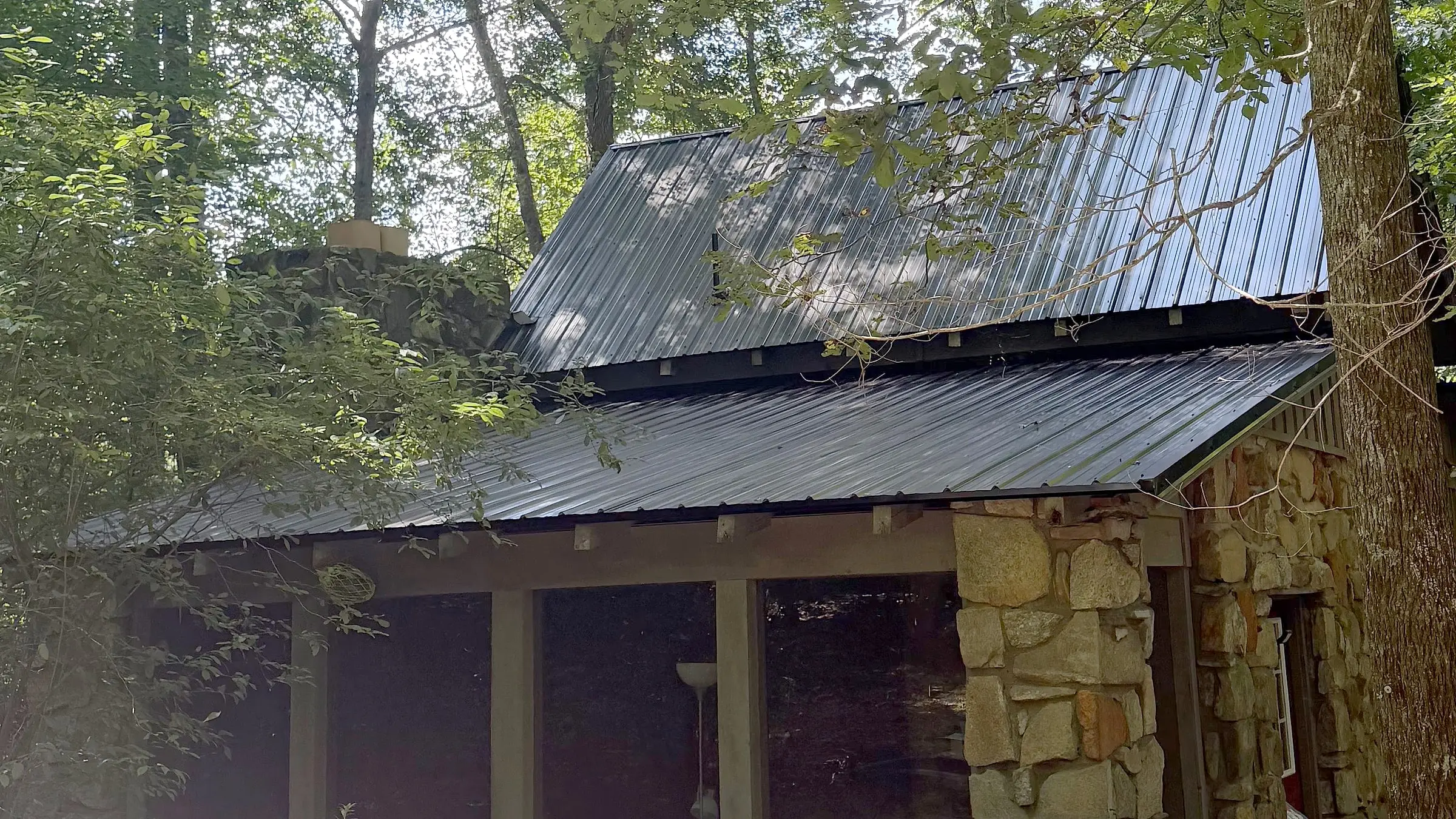 Black exposed-fastener metal roof installed by Iron Ridge Roofing on a stone and timber cabin in the woods