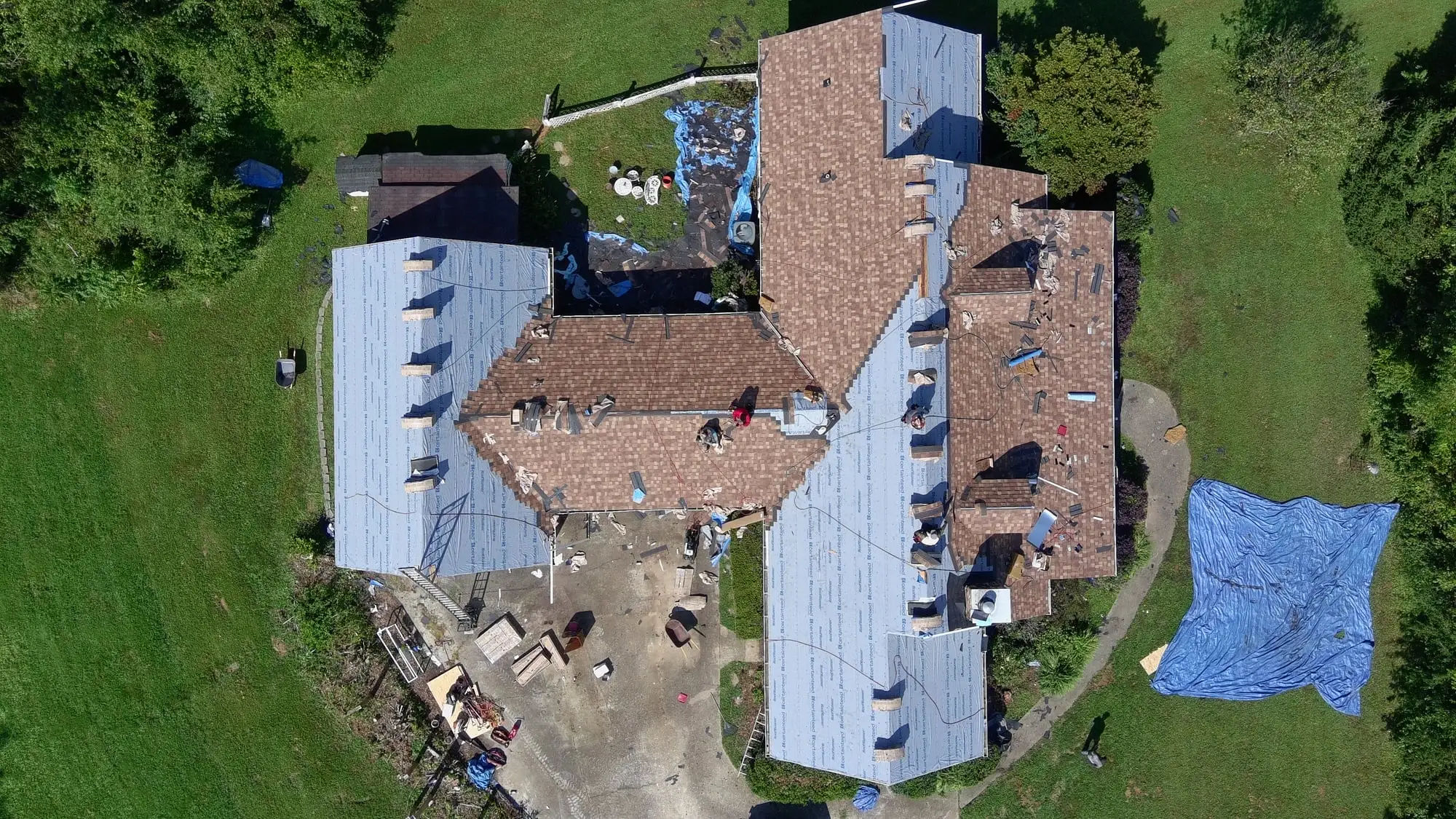 Top-down drone view of an Iron Ridge roof replacement in progress, with tarps protecting the yard