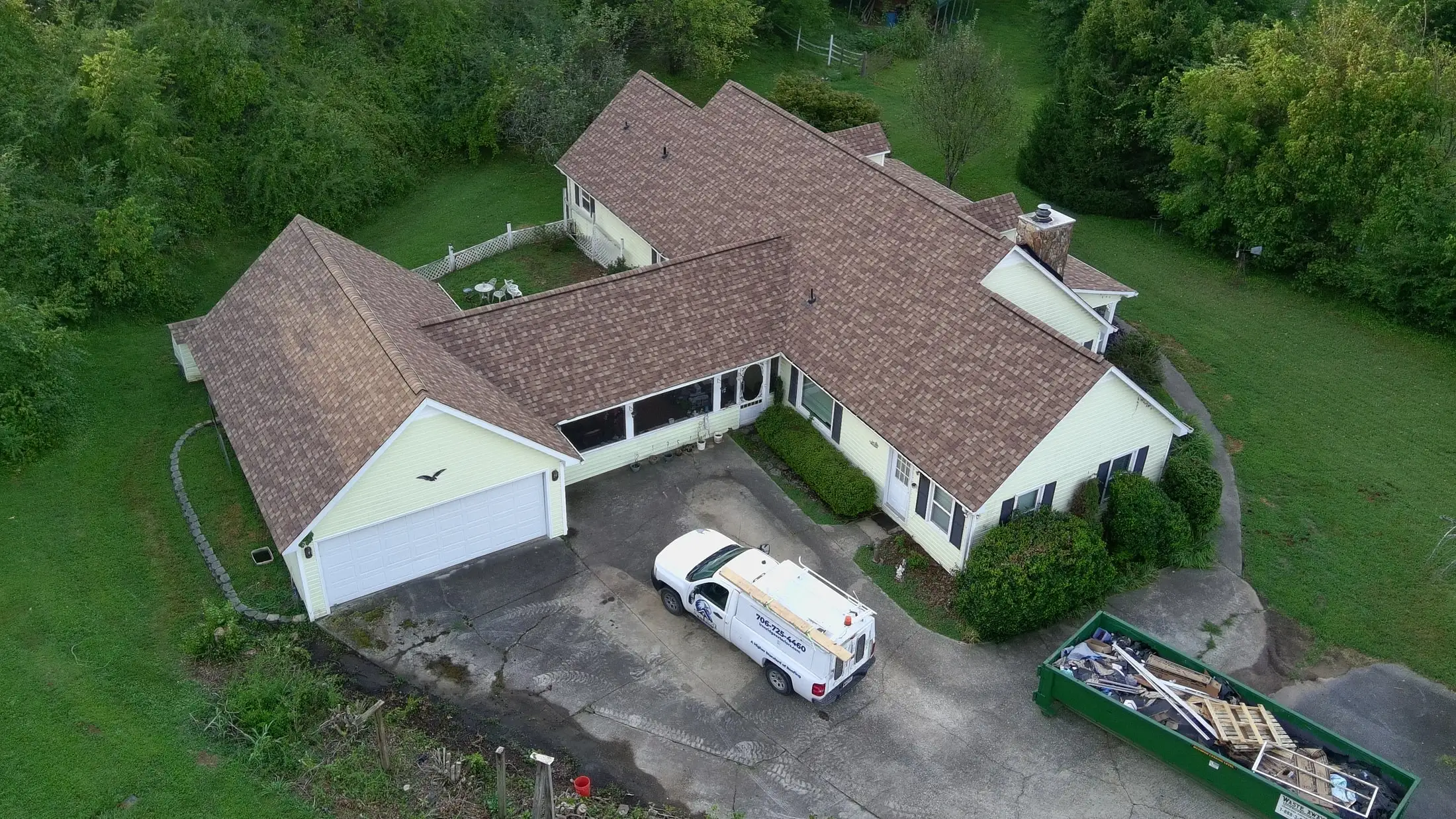 Aerial view of a home with a new brown shingle roof surrounded by trees