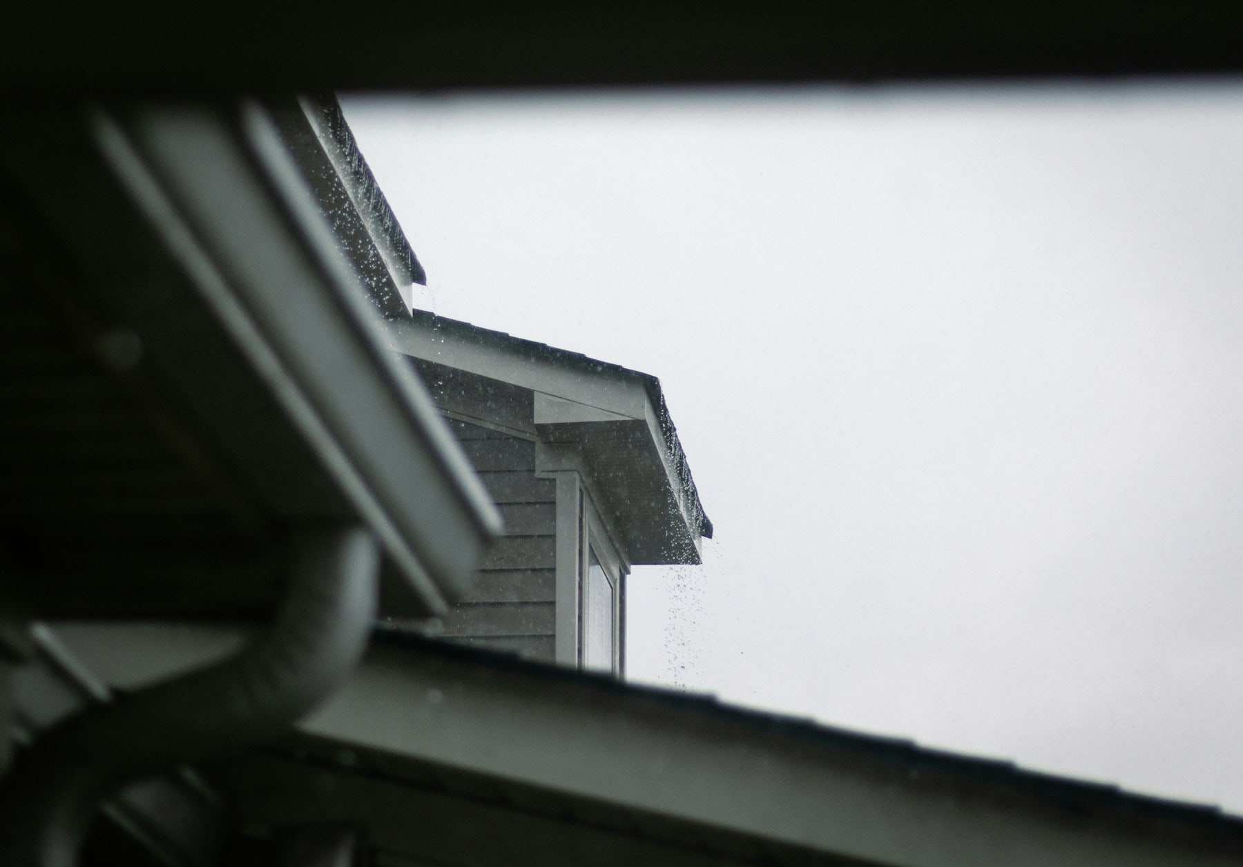 House roofline with a gutter and downspout on a grey, rainy day