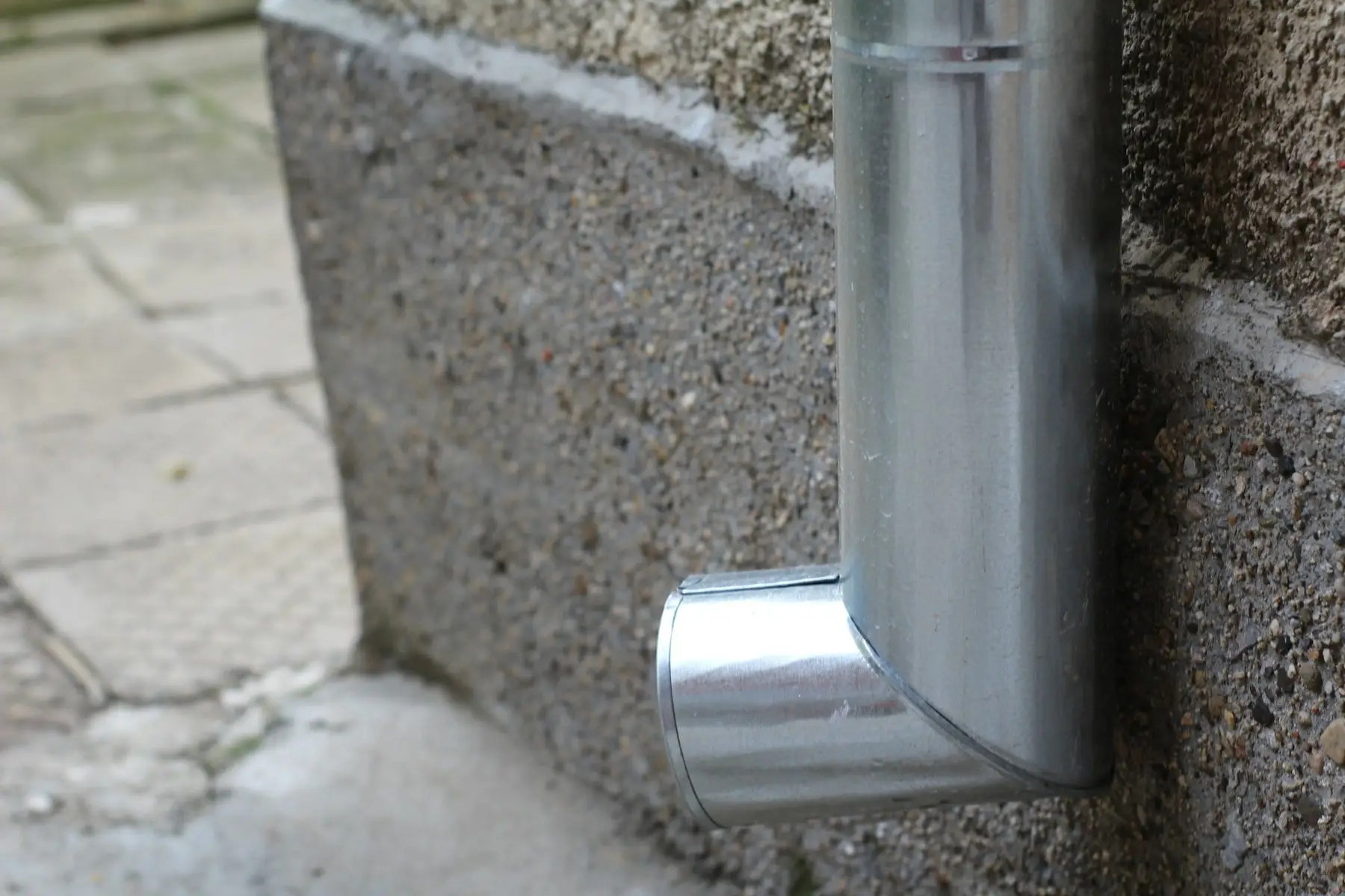 Close-up of a metal downspout elbow against a wall