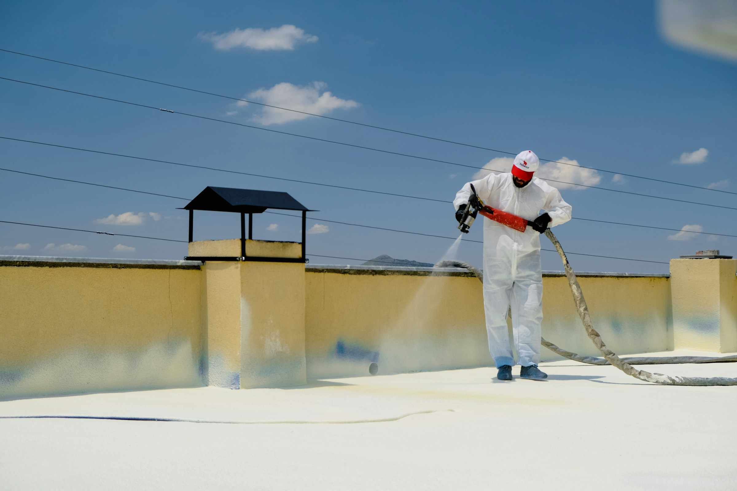 Roofer in a protective suit spraying a white coating onto a flat roof