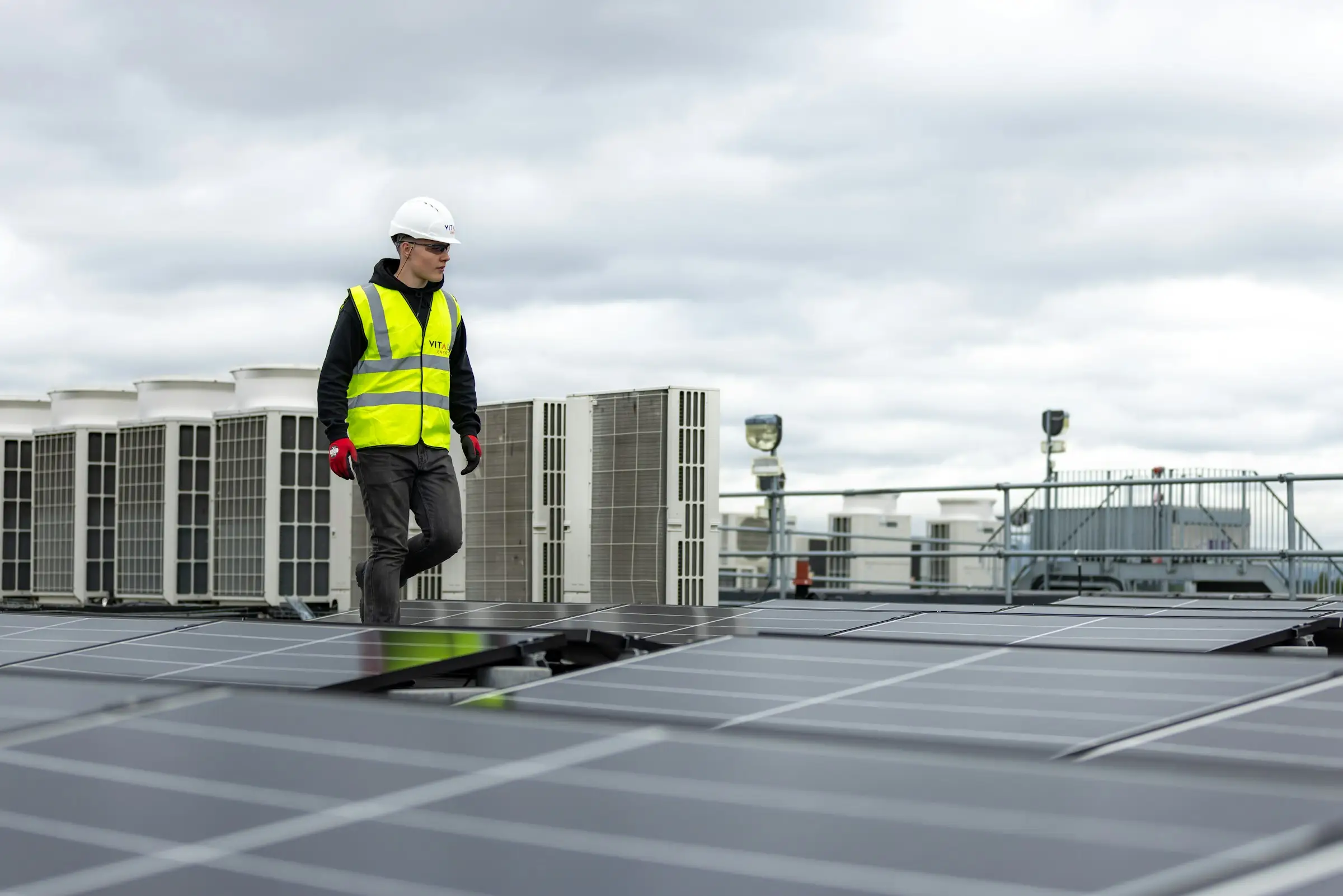 Roofer in a hard hat and safety vest walking across a commercial roof