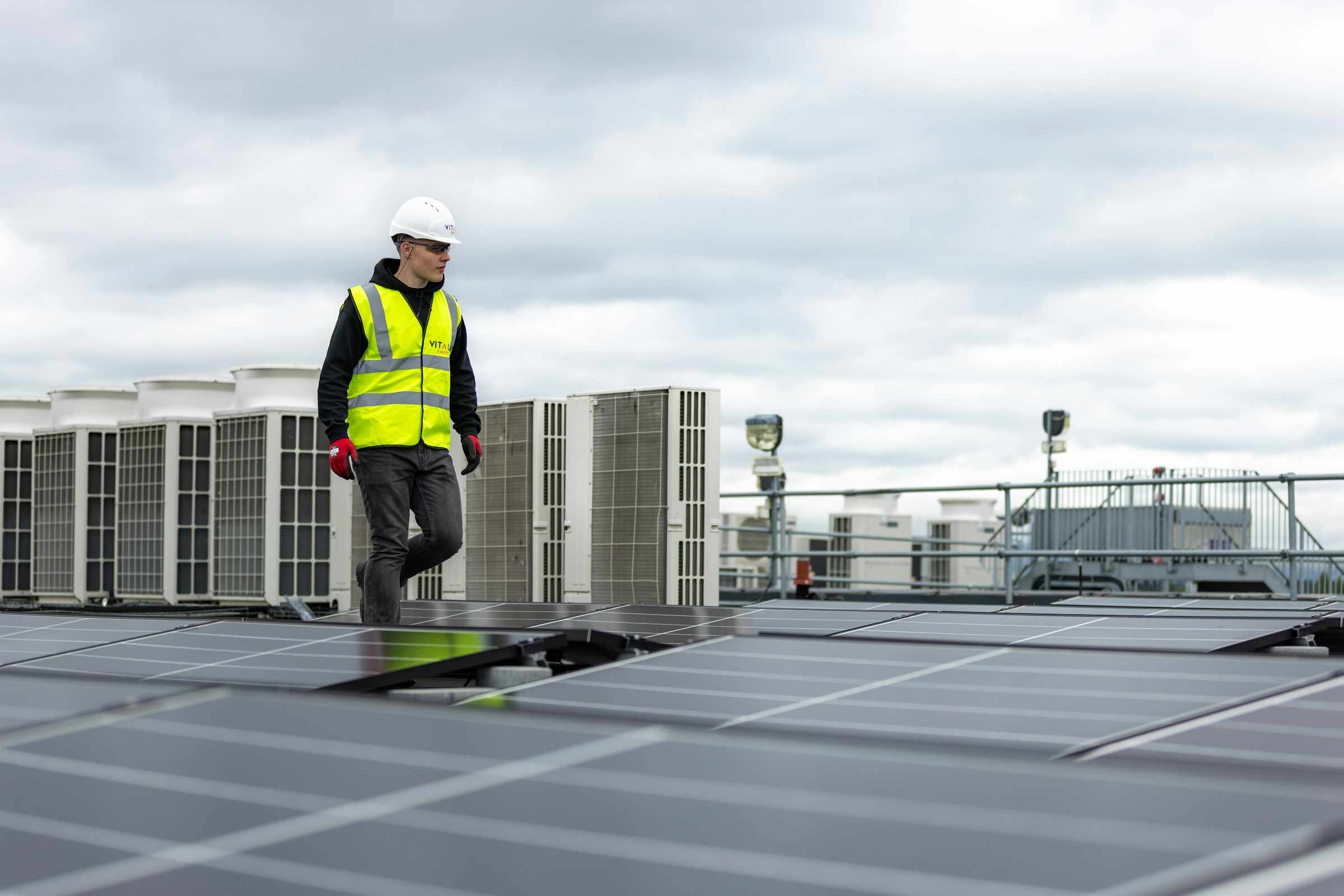 Roofer in a hard hat and safety vest walking across a commercial roof